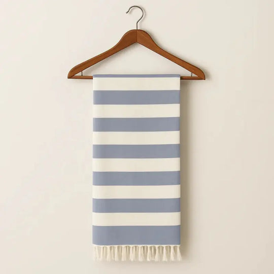 Striped towel with blue and white stripes hanging on a wooden hanger against a beige wall.