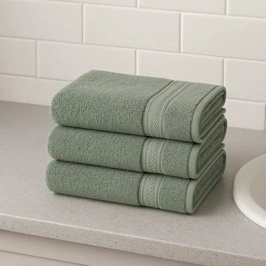 Three folded green towels on a bathroom counter with a tiled wall background