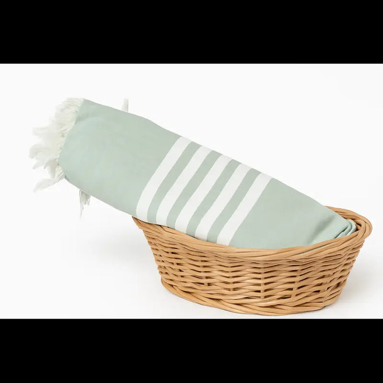 Green striped towel with white tassels in a wicker basket on a white background