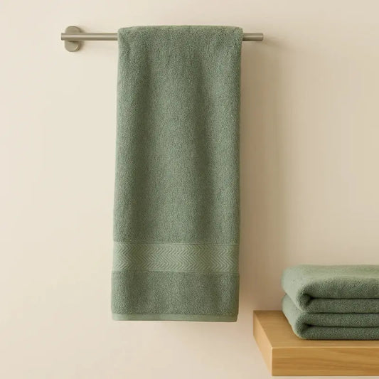 Green towel hanging on a rack with another folded towel on a wooden surface against a beige wall.