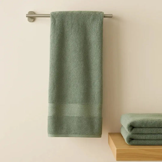 Green towel hanging on a rack with another folded towel on a wooden surface against a beige wall.