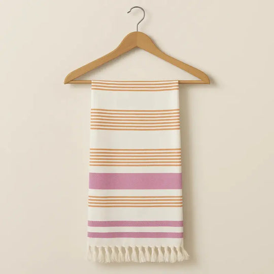 Striped towel with fringes on a wooden hanger against a beige background