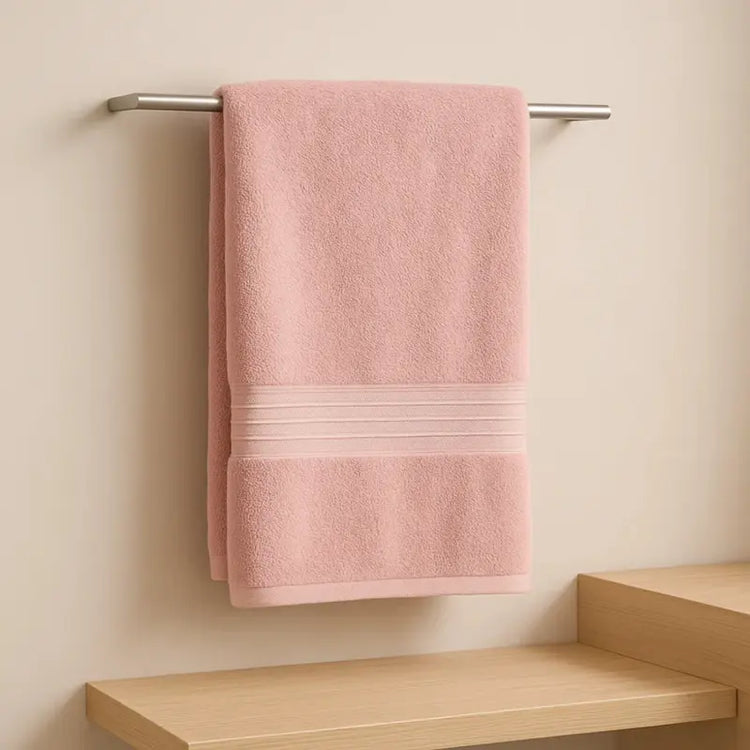 Pink towel hanging on a silver towel rack against a beige wall with a wooden shelf below.