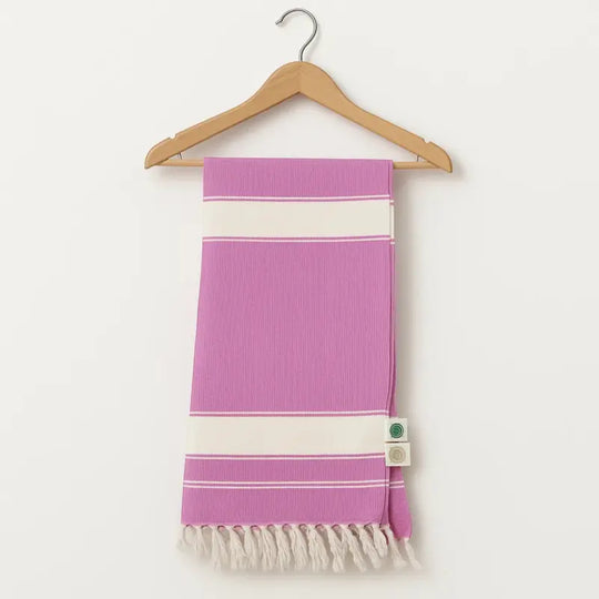 Purple towel with white stripes and fringes on a wooden hanger against a white background