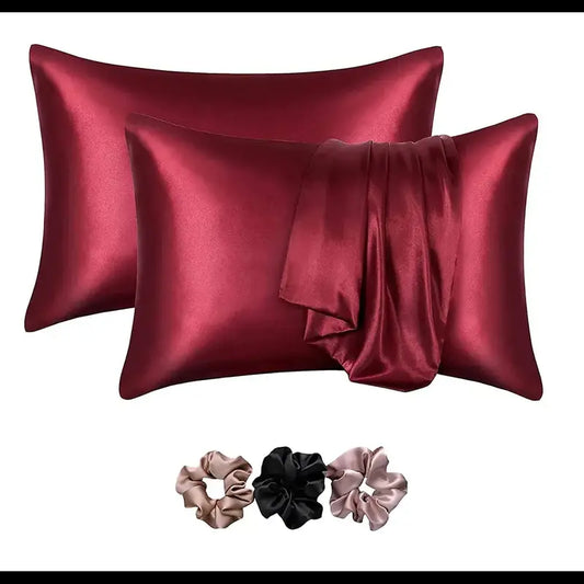 Two red satin pillowcases with three matching scrunchies on a white background