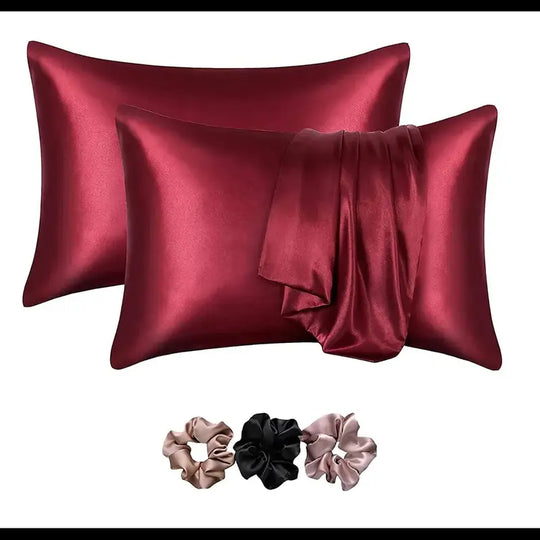 Two red satin pillowcases with three matching scrunchies on a white background