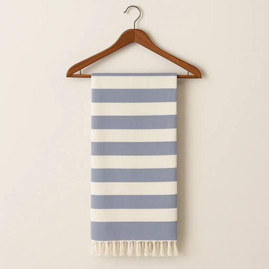 Striped towel with blue and white stripes hanging on a wooden hanger against a beige background