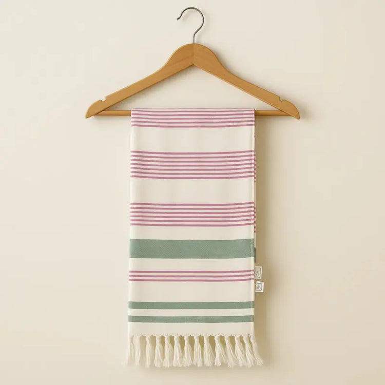 Striped towel with pink and green stripes on a wooden hanger against a beige background