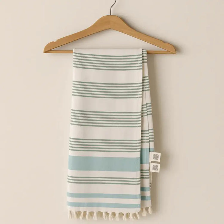 Striped towel with tassels hanging on a wooden hanger against a beige wall.