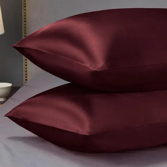 Two burgundy satin pillows on a bed with a neutral background
