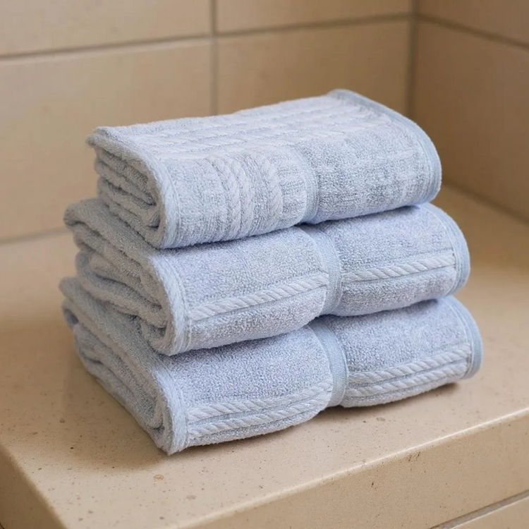 Stack of folded light blue towels on a beige surface with tiled wall background