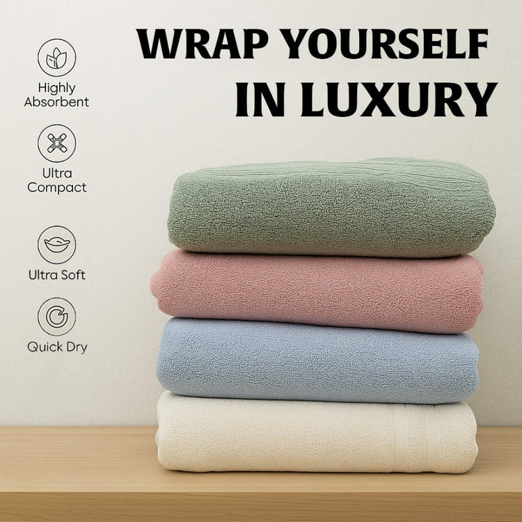 Stack of four towels in green, pink, blue, and white with text 'Wrap Yourself in Luxury' and features on a light background.